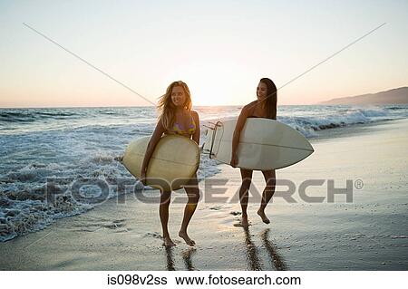 Stock Photograph - Female surfers by the sea at sunset. Fotosearch