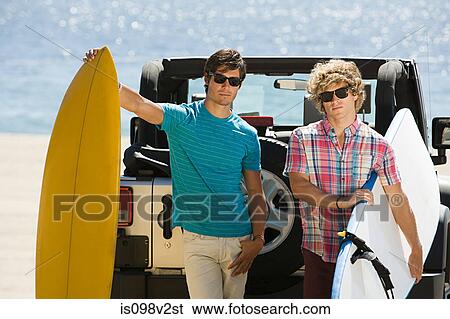 Stock Photograph - Two young men by SUV with surfboards. Fotosearch