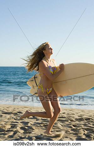 Stock Image - Young woman running with surfboard. Fotosearch