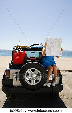 Stock Photo - Young woman sitting on vehicle looking at map. Fotosearch