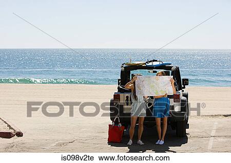 Stock Image - Young women by vehicle, looking at map. Fotosearch