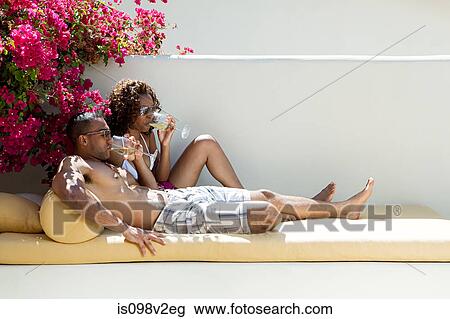 Stock Image - Couple drinking wine and relaxing on lounger. Fotosearch