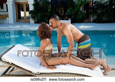 Stock Image - Couple kissing on sun lounger by pool. Fotosearch