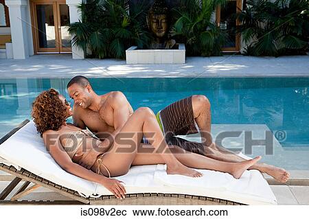 Stock Image - Couple lying on sun lounger by pool. Fotosearch