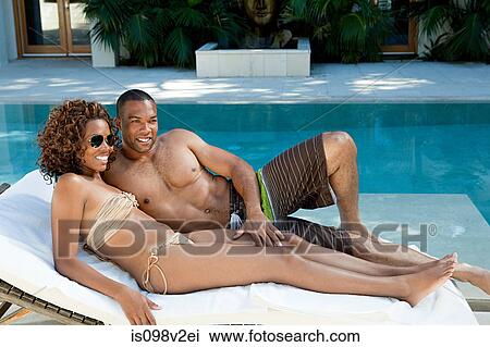 Stock Image - Couple lying on sun lounger by pool. Fotosearch
