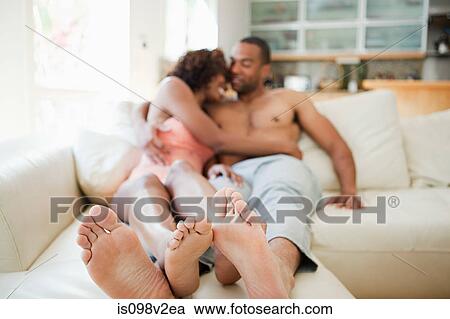 Stock Image - Couple on sofa, focus on feet in foreground. Fotosearch