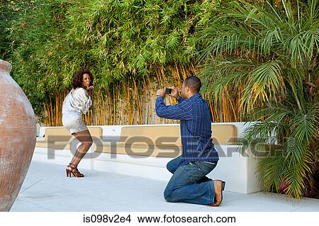 Picture - Man taking a picture of girlfriend as she blows a kiss to camera. Fotosearch