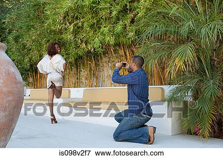 Stock Photo - Man taking a picture of girlfriend as she poses for camera. Fotosearch