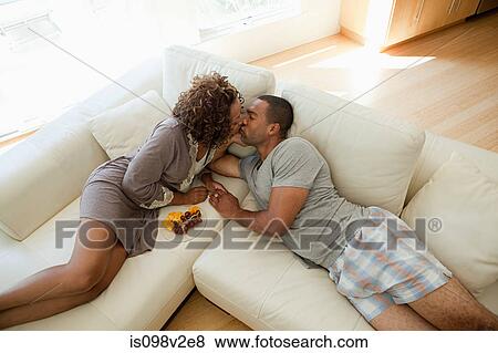 Stock Photo - Young couple kissing on sofa, high angle view. Fotosearch