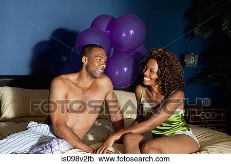 Stock Image - Young couple on bed with balloons in background. Fotosearch