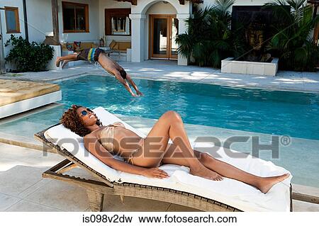 Stock Photo - Young on lounger and man diving into pool. Fotosearch