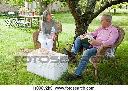 Mature couple outdoors, man reading book View Large Photo Image Stock Image - Mature couple outdoors, man reading book. Fotosearch