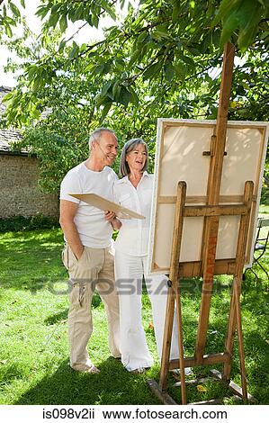 Stock Image - Mature couple, woman painting at easel. Fotosearch