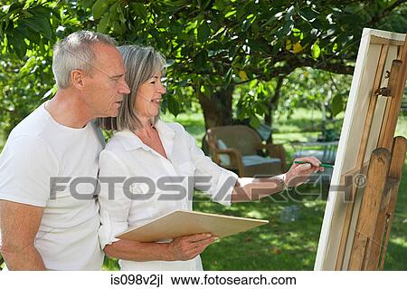 Stock Image - Mature couple, woman painting at easel. Fotosearch