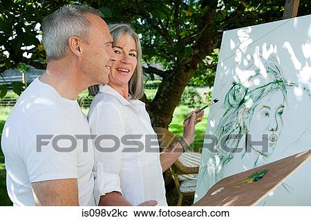 Stock Image - Mature couple, woman painting at easel. Fotosearch
