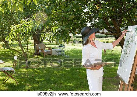 Stock Image - Mature woman painting at easel. Fotosearch