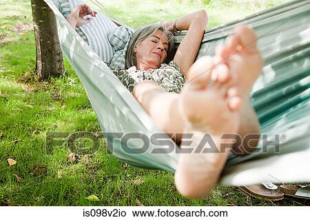 Picture - Mature woman sleeping barefoot in hammock. Fotosearch