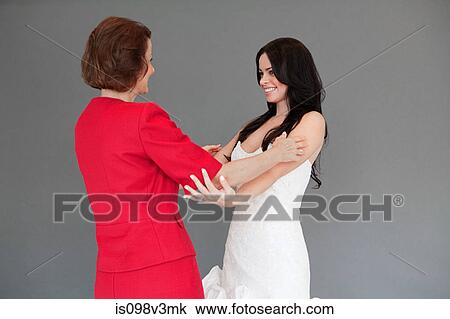 Stock Image - Daughter trying on wedding dress, embracing mother. Fotosearch