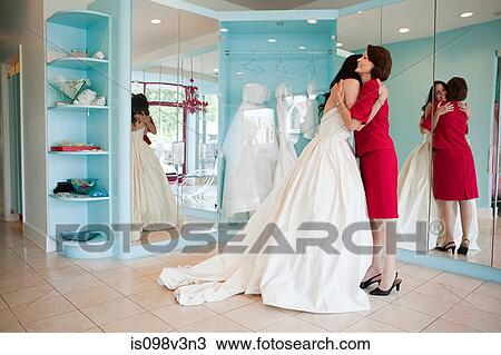 Stock Image - Daughter trying on wedding dress, embracing mother. Fotosearch