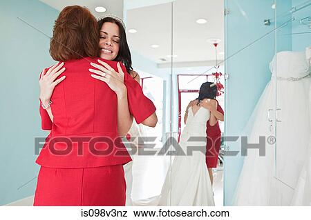 Stock Photo - Daughter trying on wedding dress, embracing mother. Fotosearch