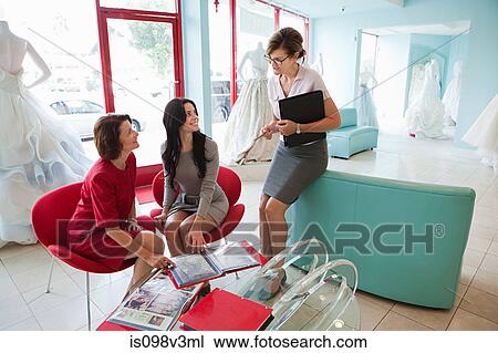 Stock Image - Mother and daughter talking to wedding dress designer. Fotosearch