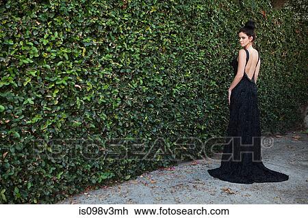 Young woman wearing black evening dress, standing by hedge View Large Photo Image Stock Image - Young woman wearing black evening dress, standing by hedge. Fotosearch