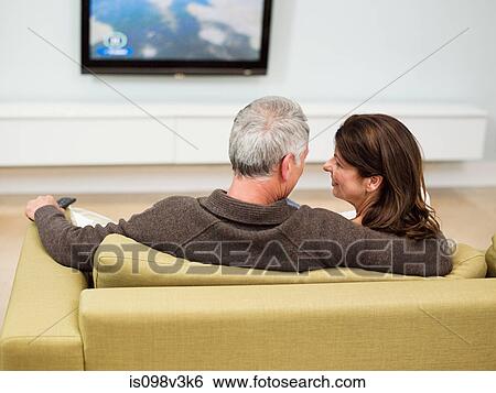 Mature couple sitting on sofa watching television View Large Photo Image Stock Photograph - Mature couple sitting on sofa watching television. Fotosearch