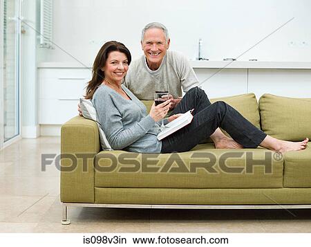 Picture - Mature couple sitting on sofa with wine. Fotosearch