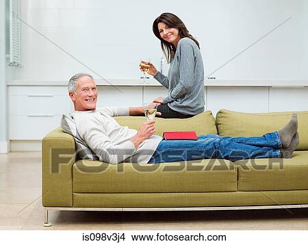 Mature couple sitting on sofa with wine View Large Photo Image Picture - Mature couple sitting on sofa with wine. Fotosearch