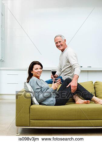 Picture - Mature couple sitting on sofa with wine. Fotosearch