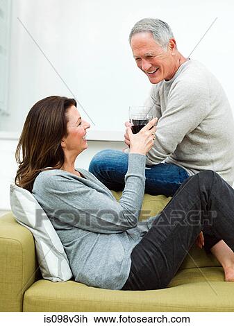 Stock Image - Mature couple sitting on sofa with wine. Fotosearch
