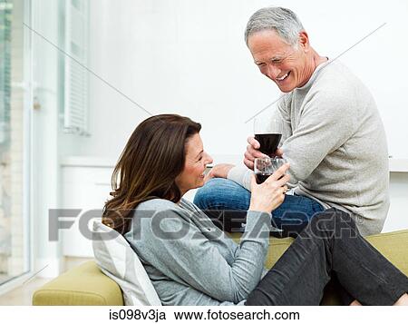 Stock Image - Mature couple sitting on sofa with wine. Fotosearch