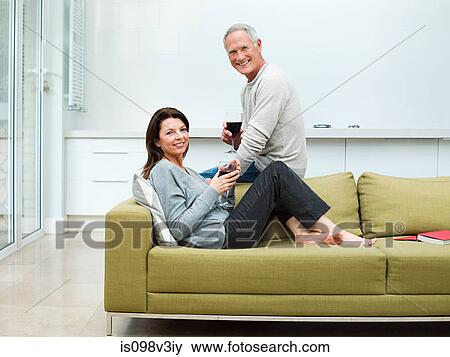 Stock Photo - Mature couple sitting on sofa with wine. Fotosearch