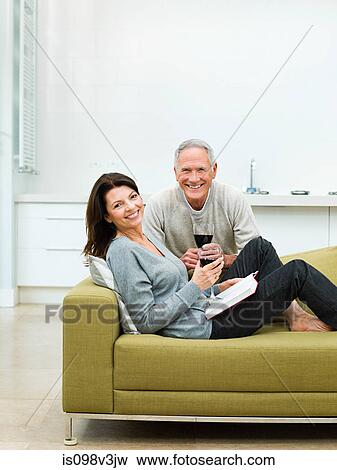 Mature couple sitting on sofa with wine View Large Photo Image Stock Photo - Mature couple sitting on sofa with wine. Fotosearch