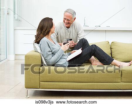 Stock Photograph - Mature couple sitting on sofa with wine. Fotosearch