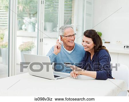 Stock Photo - Mature couple using laptop, man on telephone. Fotosearch