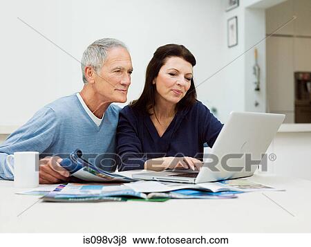 Mature couple using laptop to book vacation View Large Photo Image Stock Photo - Mature couple using laptop to book vacation. Fotosearch