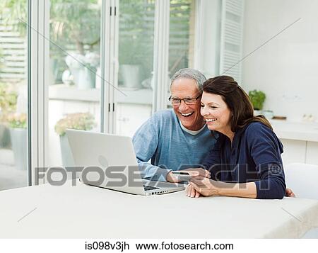Stock Image - Mature couple using laptop with credit card. Fotosearch