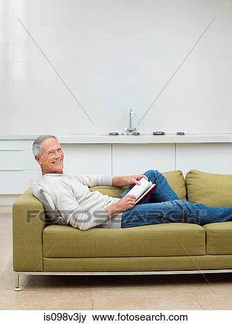 Senior man sitting on sofa reading book View Large Photo Image Stock Photo - Senior man sitting on sofa reading book. Fotosearch