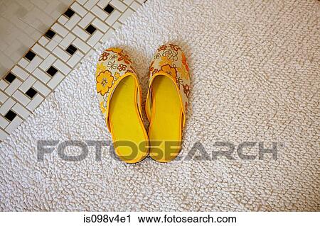 Stock Image - Pair of yellow slippers on rug. Fotosearch