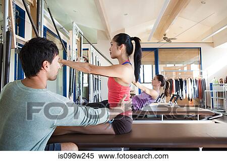 Stock Photography - Pilates instructor assisting woman. Fotosearch