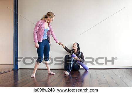 Stock Image - Woman helping another woman up from the gym floor. Fotosearch