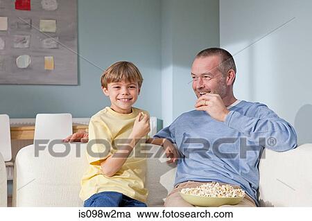 Stock Image - Father and son eating popcorn. Fotosearch