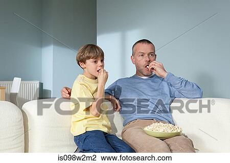 Father and son watching television eating popcorn View Large Photo Image Stock Image - Father and son watching television eating popcorn. Fotosearch