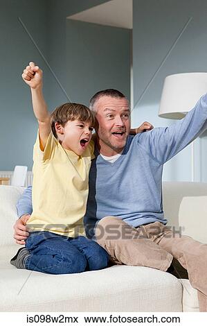 Father and son watching television cheering View Large Photo Image Stock Photo - Father and son watching television cheering. Fotosearch