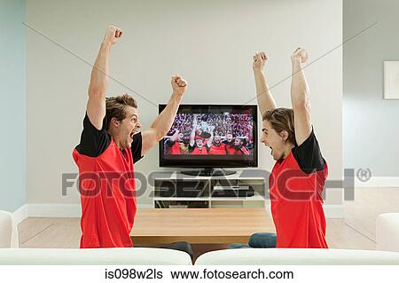 Two young men wearing football shirts watching football on television View Large Photo Image Stock Photograph - Two young men wearing football shirts watching football on television. Fotosearch