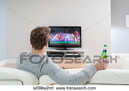 Stock Image - Young man watching football on television with beer bottle. Fotosearch
