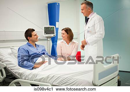 Stock Image - Wife visiting husband in hospital, talking to doctor. Fotosearch