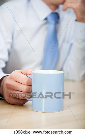 Stock Image - Office worker holding mug, close up. Fotosearch