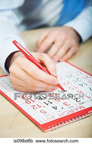 Stock Image - Office worker marking calendar with red pen. Fotosearch